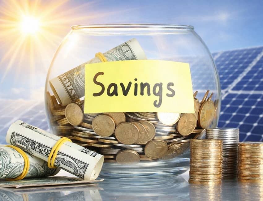 Glass savings jar filled with coins and dollar bills with yellow 'Savings' label, solar panels visible in background, stacks of coins beside the jar representing solar energy financial savings
